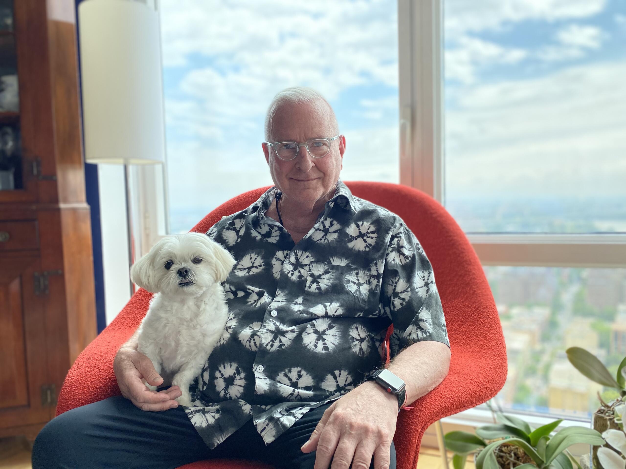 a man sitting in a red chair holding a white dog.