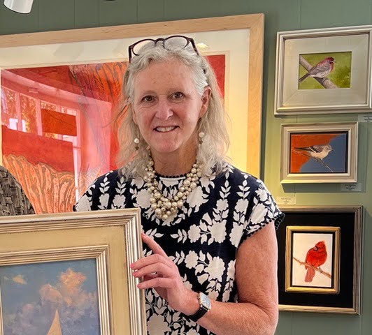 a woman holding a framed picture in front of a wall of paintings.