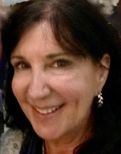 A woman with dark hair, wearing earrings, smiles at the camera in a close-up portrait.